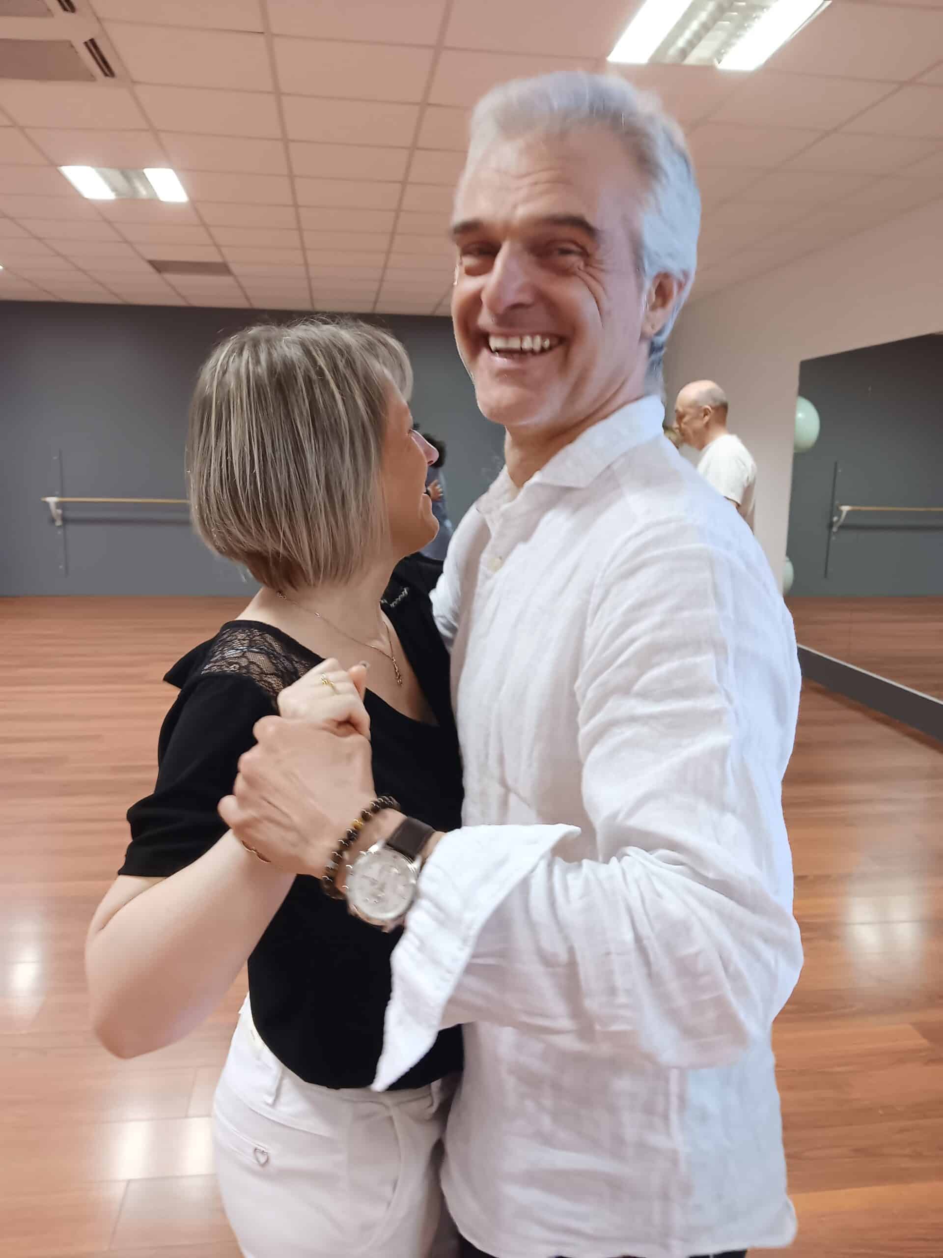 Couple d'adultes souriants pratiquant la danse de salon dans un studio avec parquet et miroirs.
