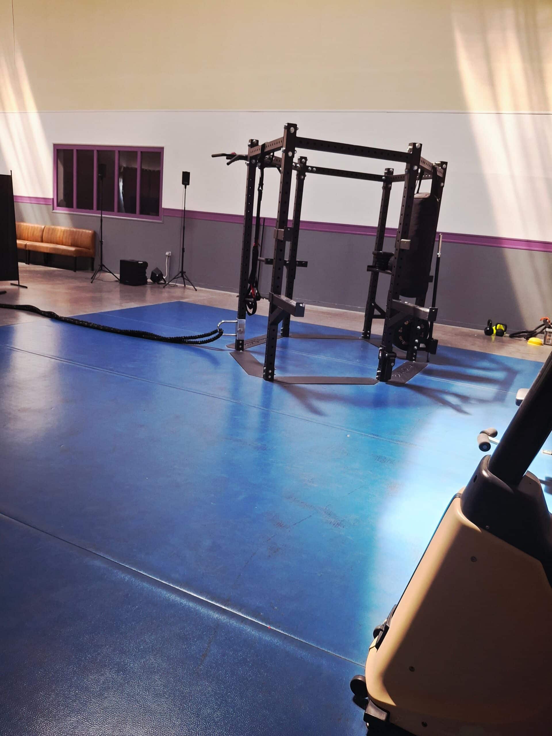 Cage de musculation noire, cordes de combat et tapis bleu dans une salle de fitness moderne.