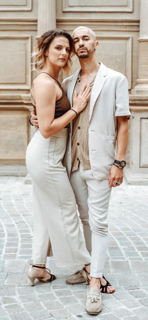 Couple élégant posant en tenue chic devant un bâtiment historique en pierre.