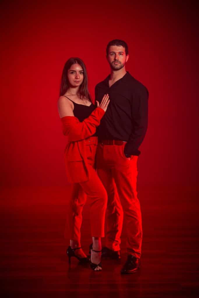 Couple en tenue rouge et noir posant avec élégance sur fond rouge.