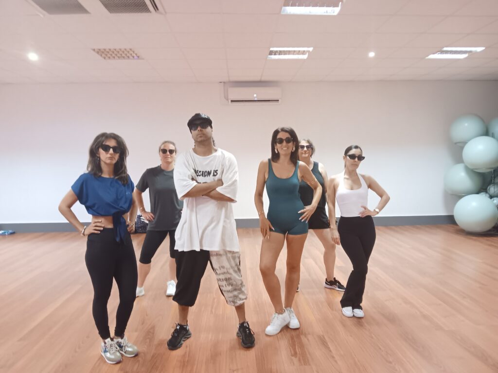 Séance de fitness : groupe de danseurs stylés en studio Groupe de fitness en lunettes de soleil au studio. Homme central t-shirt 'PASSION IS'. Pose confiante et sportive.