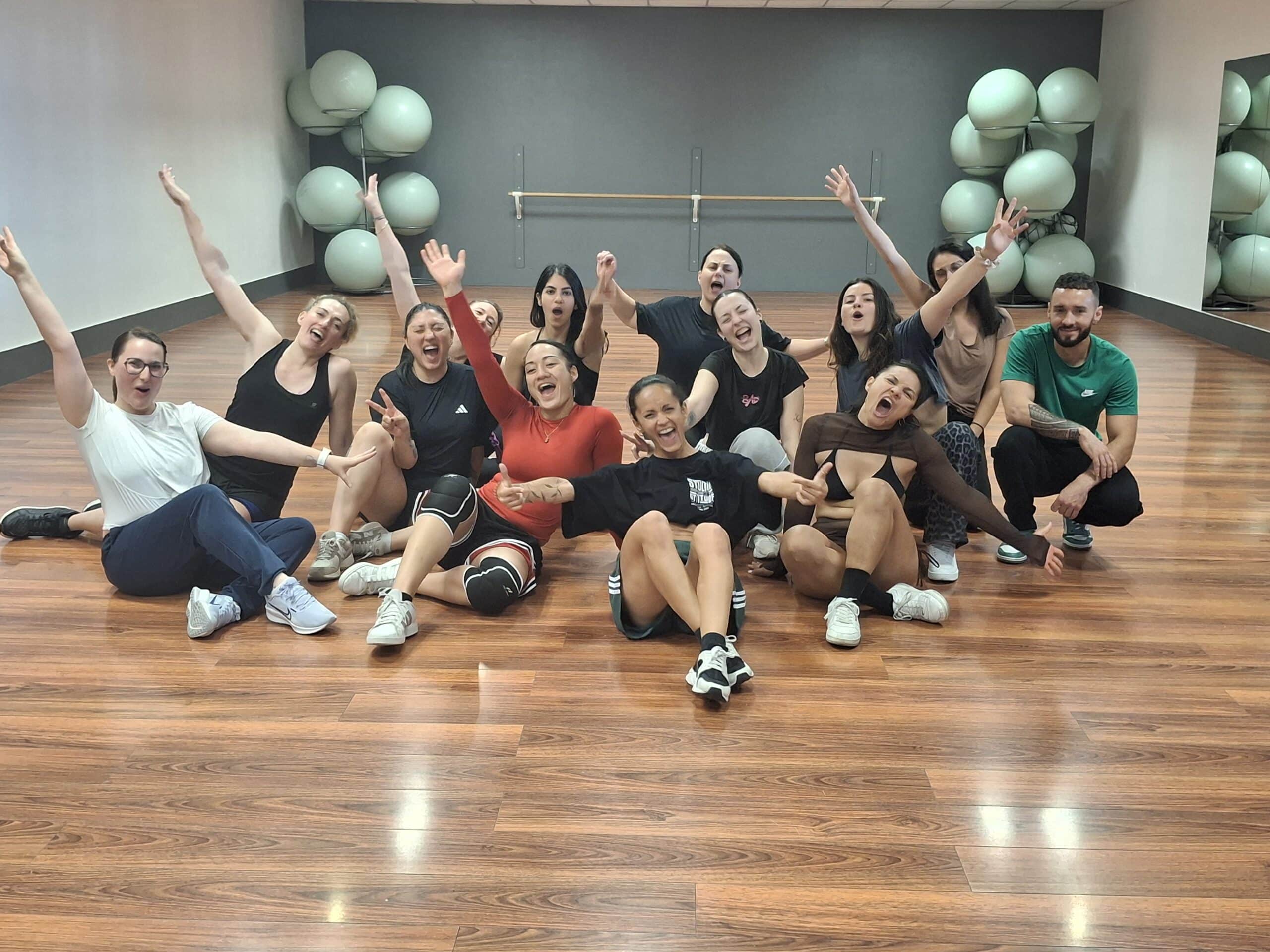 Groupe dynamique au Studio Attitude après un cours de danse, parquet et ballons de fitness en fond.