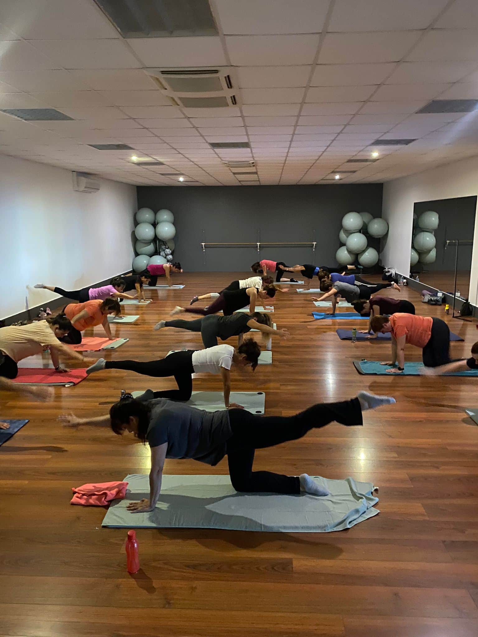 Femmes pratiquant le pilates au sol dans un studio avec parquet et ballons de gym.