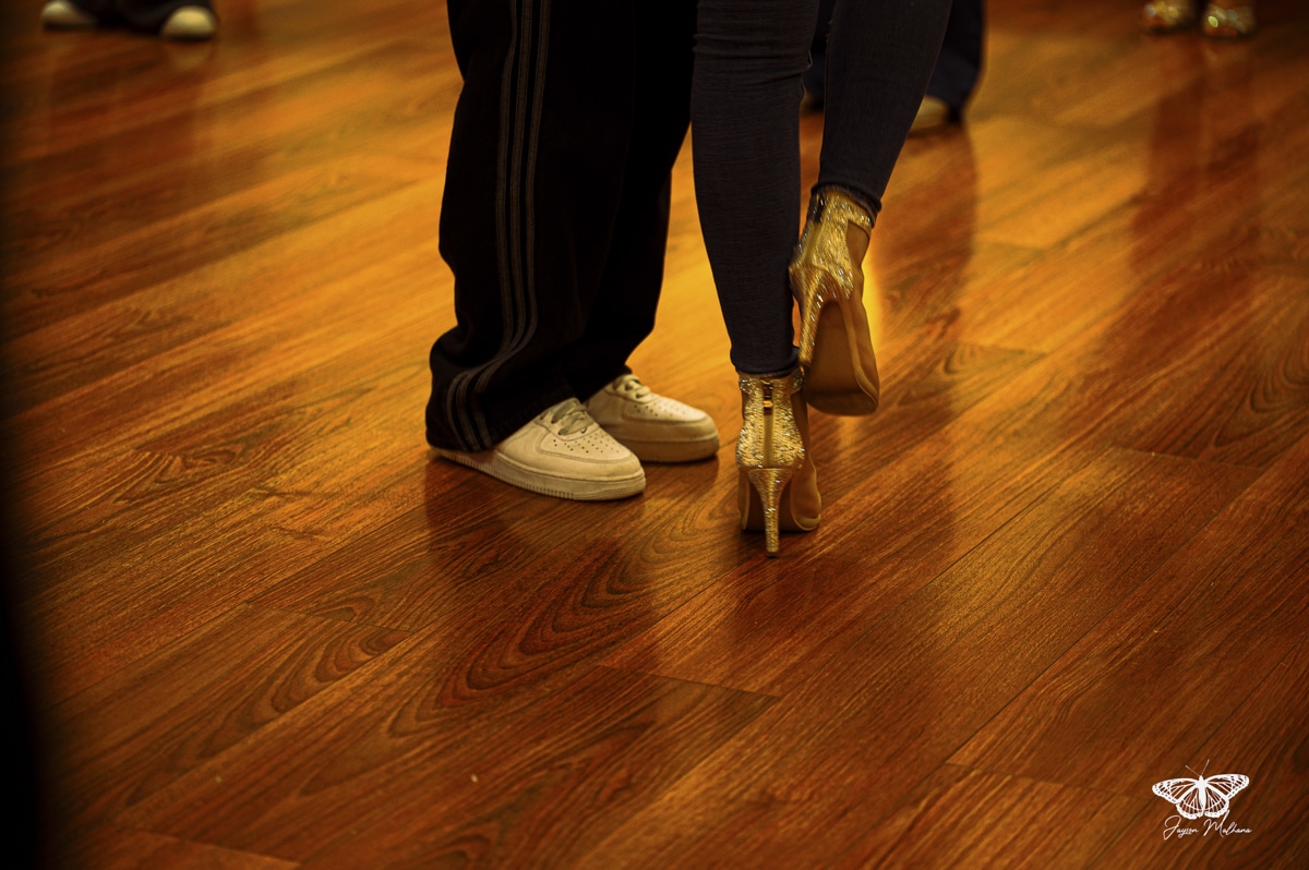 Couple dansant sur parquet : baskets blanches et bottines dorées à paillettes. Signature Jayson Mollana.