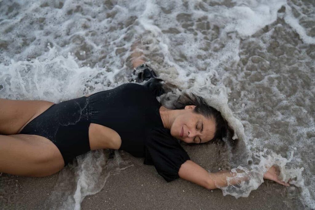 Femme en maillot noir allongée sur le sable, balayée par l'écume des vagues.