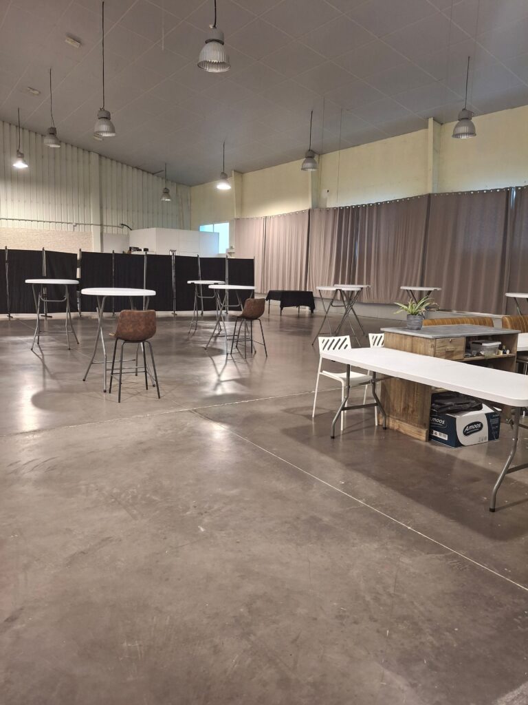 Grande salle événementielle industrielle aménagée avec tables hautes, tabourets et cloisons de séparation.