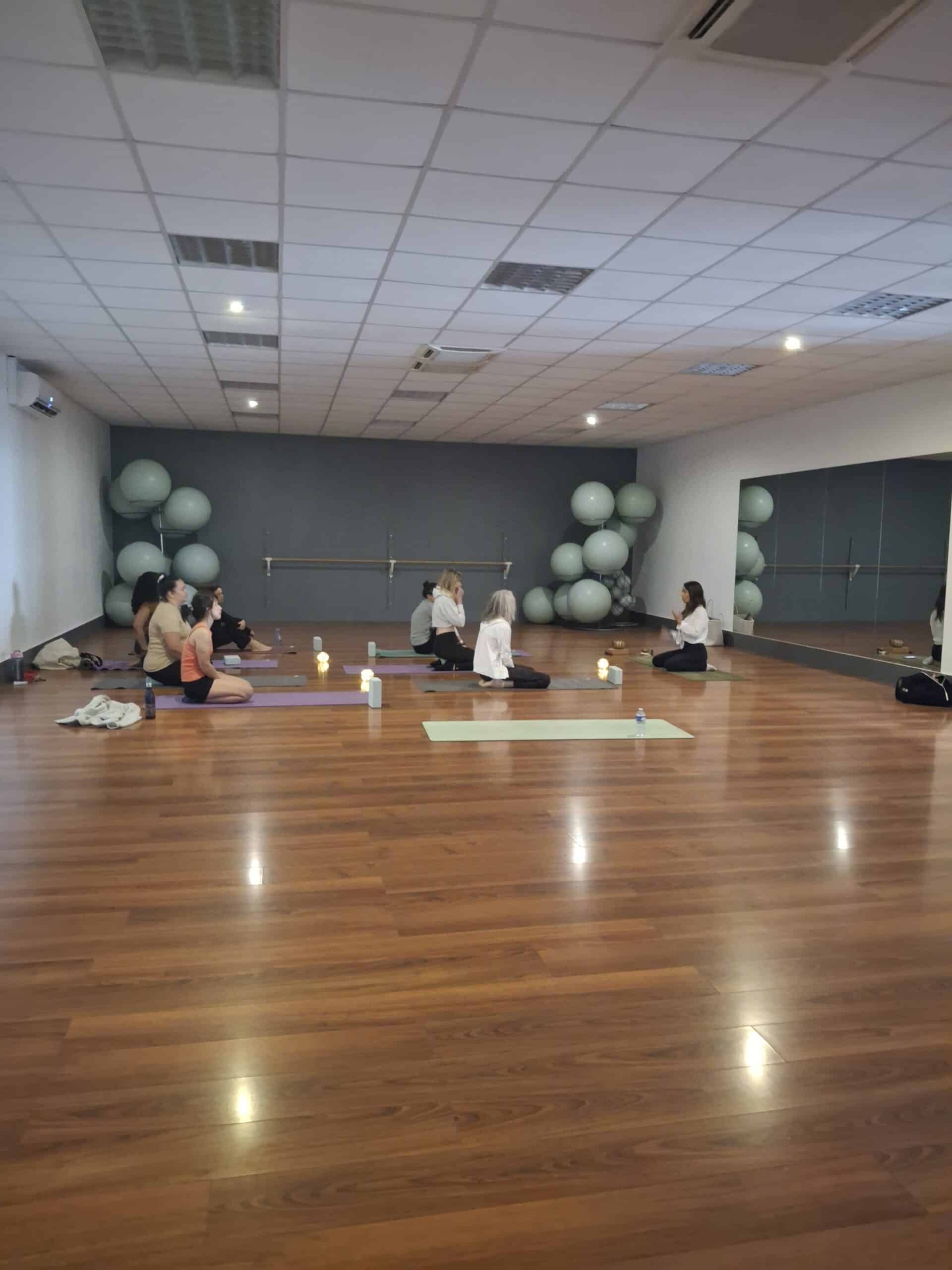 Séance de yoga et méditation en groupe dans un studio avec parquet, bougies et ballons de gym.