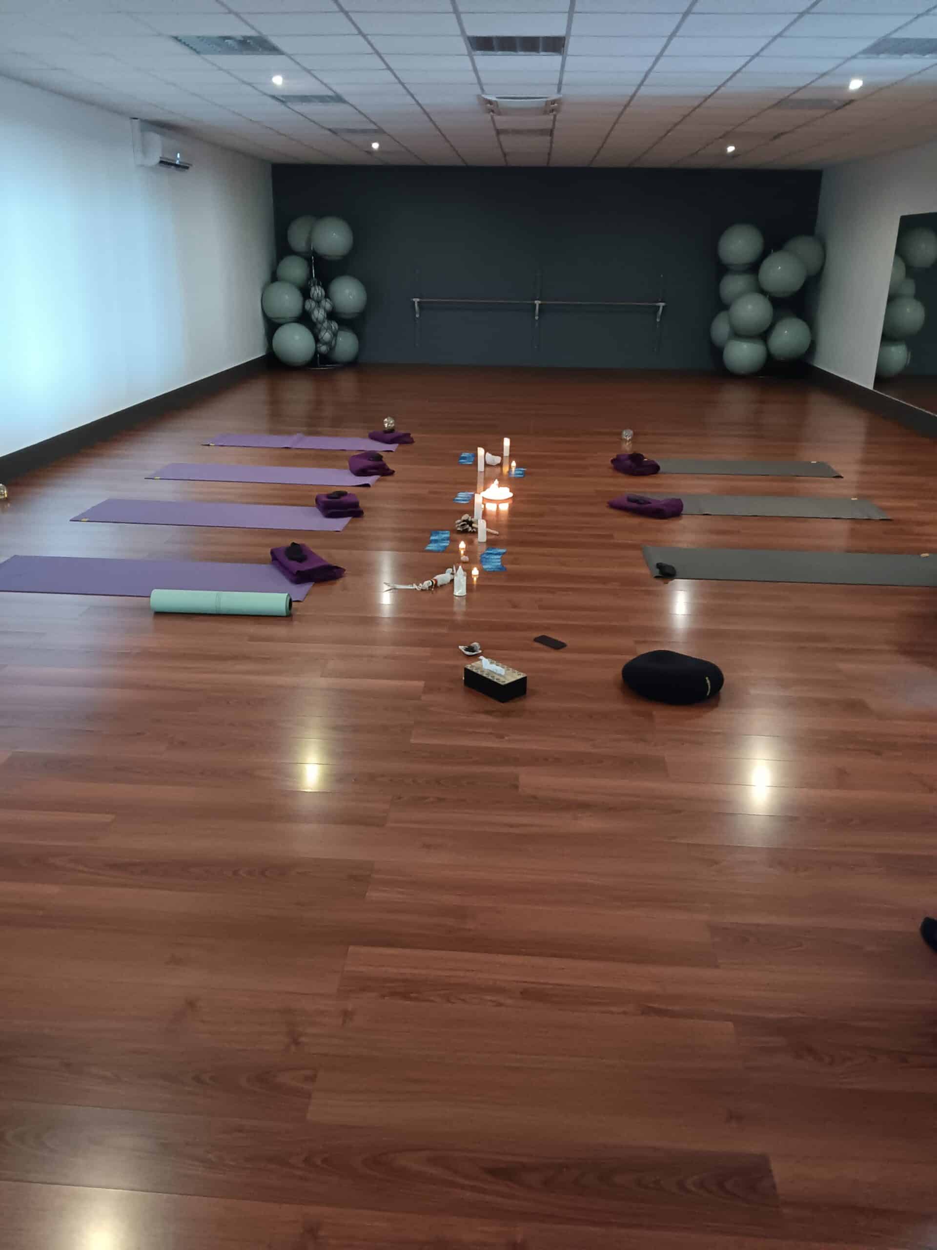Studio de yoga zen avec tapis violets, bougies centrales et ballons de gym sur parquet en bois.