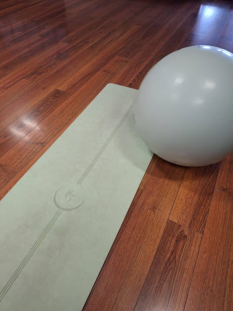 Tapis de Yoga et Ballon d'Exercice sur Sol en Bois Tapis de yoga vert à motifs et ballon de fitness blanc sur un parquet en bois.